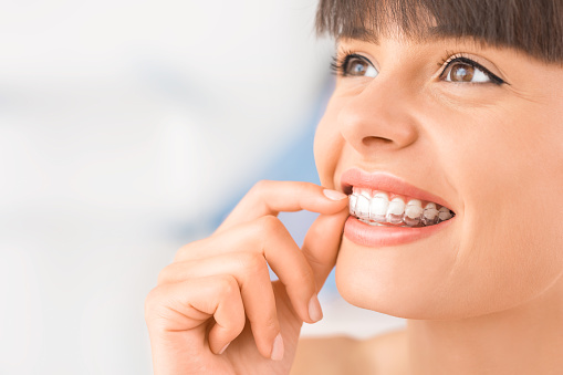 woman smiling while putting on clear aligners from Brush & Floss Dental Center in Stratford, CT